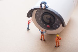 Miniaturarbeiter stehen an einer großen Überwachungskamera und symbolisieren Wartungsservice